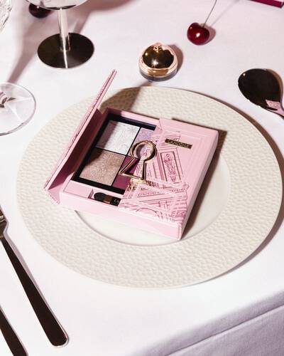 Růžova paleta očnich stinů Lancome se zlatym motivem kličove dirky, elegantně umistěna na bilem jidelnim taliři.