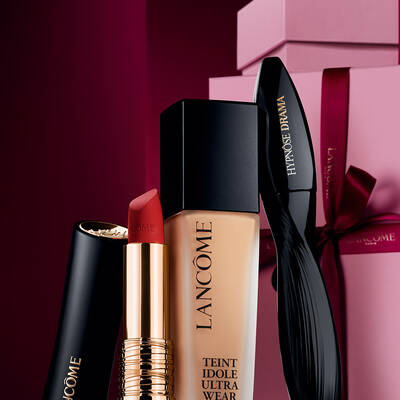 Elegantni zatiši matne rtěnky Lancome L’Absolu Rouge, make-upu Teint Idole Ultra Wear a řasenky Hypnose Drama na luxusnim tmavě červenem svatečnim pozadi.