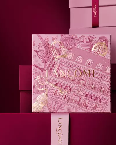Elegantni kompozice růžovych a tmavě vinovych darkovych krabiček Lancome, uprostřed s krabičkou zdobenou zlatymi ilustracemi pařižske architektury.