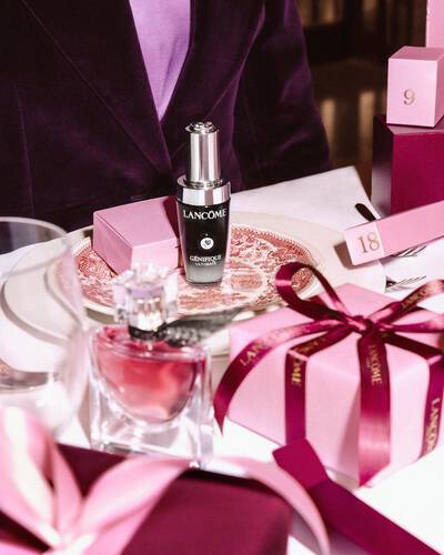 Produkty Lancome a růžove darkove krabičky naaranžovane na slavnostně prostřenem stole.