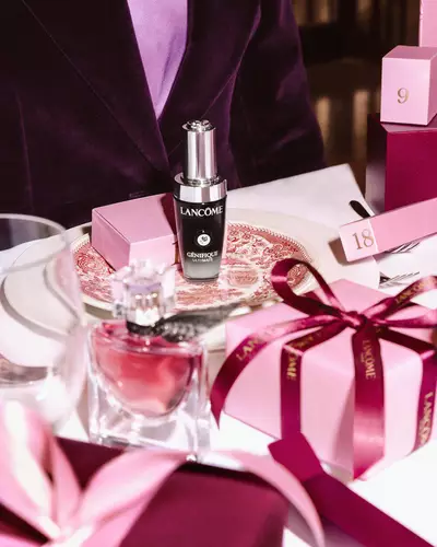 Produkty Lancome a růžove darkove krabičky naaranžovane na slavnostně prostřenem stole.