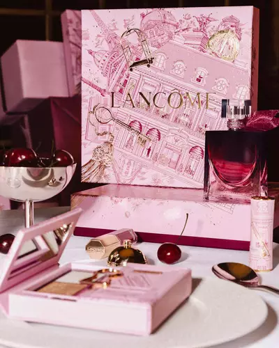 Slavnostni prezentace svatečni kolekce Lancome na stole s velkou ilustrovanou růžovou darkovou krabičkou, parfemem, produkty dekorativni kosmetiky a čerstvymi třešněmi.