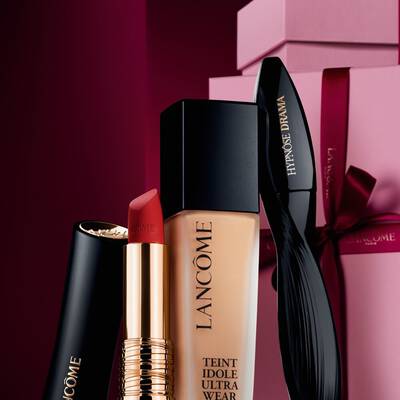 Elegantni aranžma matne rtěnky Lancome L'Absolu Rouge, make-upu Teint Idole Ultra Wear a řasenky Hypnose Drama na luxusnim tmavě červenem svatečnim pozadi.