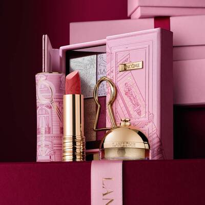 Pečlivě sestavena svatečni darkova sada Lancome s rtěnkou, paletou očnich stinů a zlatymi kosmetickymi produkty vystavenymi na dekorativnim růžovem pouzdře.