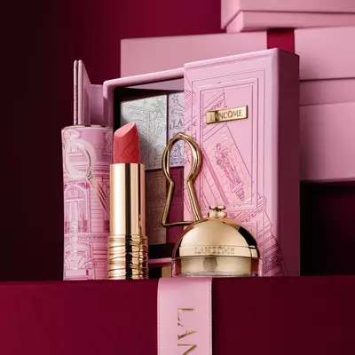 Pečlivě sestavena svatečni darkova sada Lancome s rtěnkou, paletou očnich stinů a zlatymi kosmetickymi produkty vystavenymi na dekorativnim růžovem pouzdře.