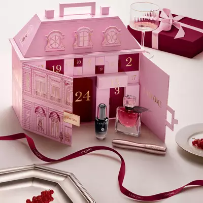 Otevřeny růžovy adventni kalendař Lancome ve tvaru pařižskeho palace s vystavenymi kosmetickymi produkty a červenou stuhou.