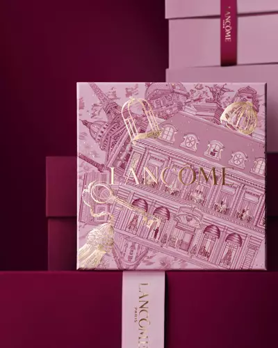Obrazek růžove vanočni darkove krabičky Lancome před hromadou růžovych a tmavě červenych darkovych krabiček na tmavě červenem pozadi.
