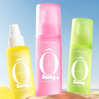 Tři Lancome Juicy Hair & Body Mists v zařivě žlute (O Zenith), růžove (O Oui) a zelene (O Cool) barvě položene na pisečne plaži.
