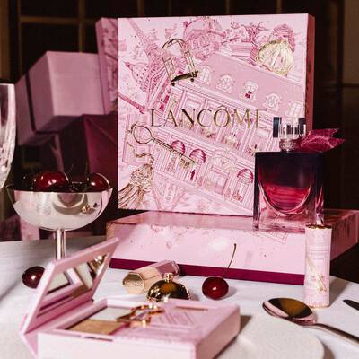 Svatečni kolekce Lancome naaranžovana na stole, včetně velke růžove darkove krabičky s ilustracemi, parfemu, kosmetickych produktů a čerstvych třešni.