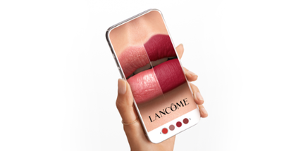 Ruka držici smartphone s aplikaci ukazujici čtyři odstiny rtěnky značky Lancome na rtech.