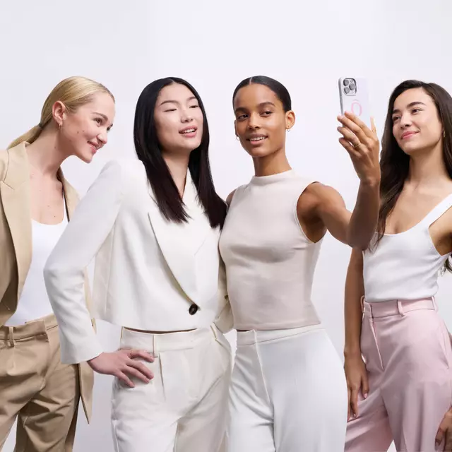 Skupina čtyř žen v elegantnim oblečeni se usmiva a fotografuje se mobilem.