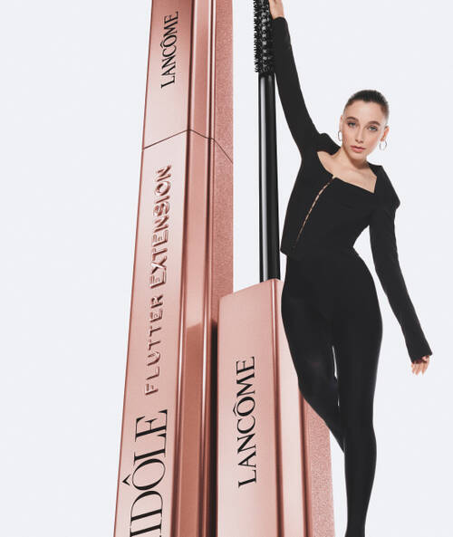 Mlada žena v černem oblečeni stoji vedle růžoveho obalu řasenky Lancome Idole Flutter Expression.