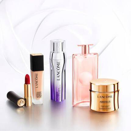 Sada kosmetiky značky Lancome, zahrnujici rtěnku, serum, parfem a krem, umistěna na střibrnem povrchu.