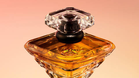 A close-up of an elegant perfume bottle with a diamond-shaped cap, filled with golden liquid, set against a soft gradient background.