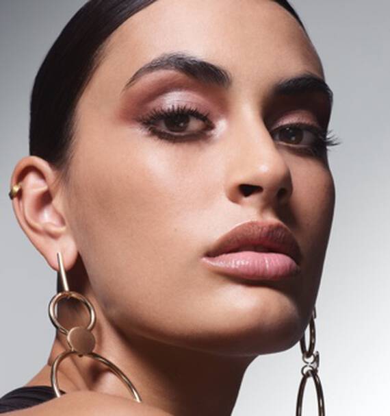 Mlada žena s vyraznym ličenim a velkymi zlatymi naušnicemi se diva přimo do kamery.
