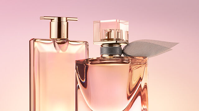 Two elegant perfume bottles are prominently displayed against a soft pink background. One bottle has a sleek rectangular shape, while the other is more rounded with a decorative accent.