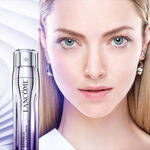 Žena s jemnou pleti a světlymi vlasy stoji vedle lahve pleťoveho sera Lancome.