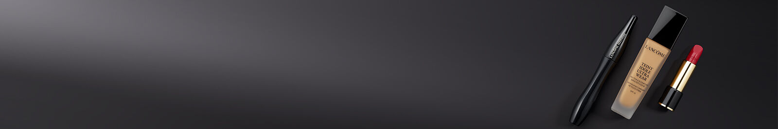 A collection of cosmetics featuring a black eyeliner, a bottle of foundation, and a red lipstick set against a sleek, dark background.