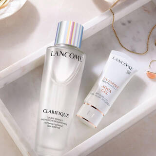 A minimalist display featuring Lancome skincare products, including a serum and cream, arranged on a marble surface alongside delicate jewelry items.