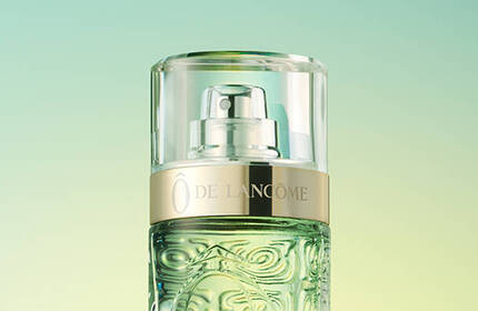 A close-up of a perfume bottle with a gold cap against a soft gradient background in green tones.