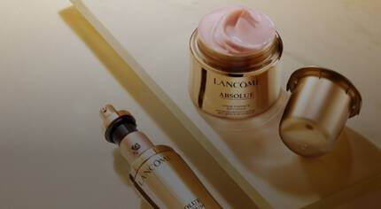 Popis produktu značky Lancome: Skleněna nadoba s růžovym kremem a flakon s serem na zlatem podkladu.