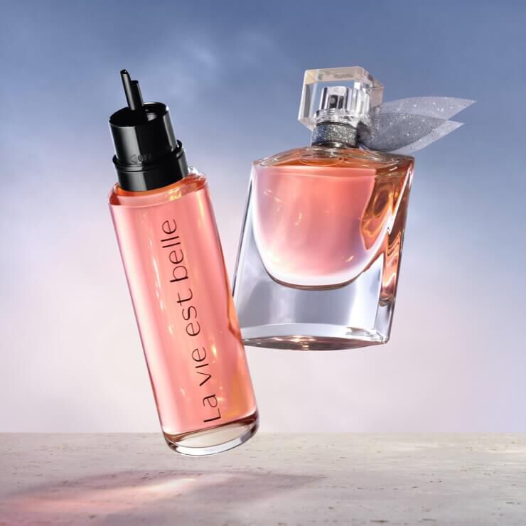 Dva flakony parfemů na světle modrem pozadi, jeden s napisem "la vie est belle".