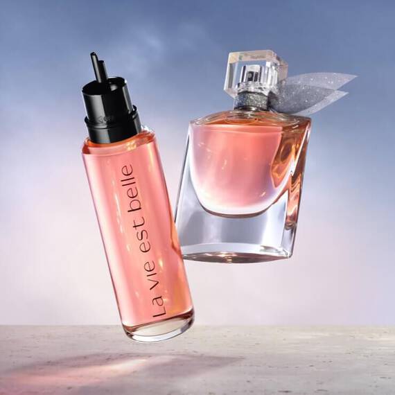 Dva flakony parfemů na světle modrem pozadi, jeden s napisem "la vie est belle".