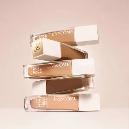 Na obrazku jsou čtyři lahvičky make-upu značky Lancome, uspořadane do sloupu na hladkem, světlem pozadi.
