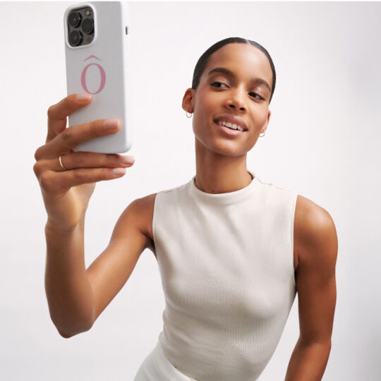 Žena s kratkym učesem se usmiva při natačeni selfie s telefonem v ruce.