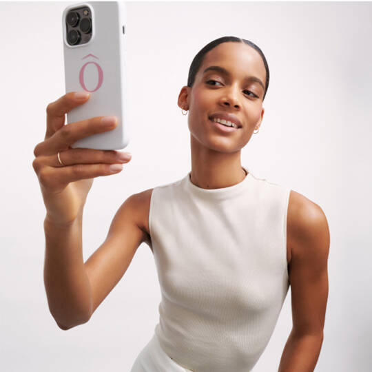 Žena s kratkym učesem se usmiva při natačeni selfie s telefonem v ruce.