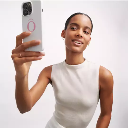 Žena s kratkym učesem se usmiva při natačeni selfie s telefonem v ruce.
