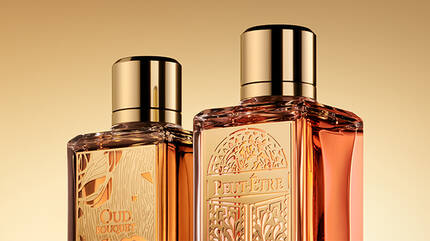 Two elegant perfume bottles with golden caps, displayed against a warm golden background.