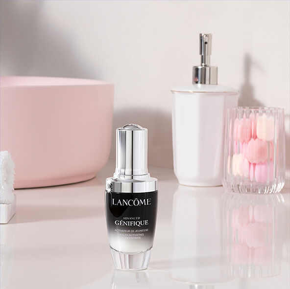 Serum Lancome Genifique na elegantnim stole se skleněnym vazičkou s růži a dalšimi dekorativnimi prvky.