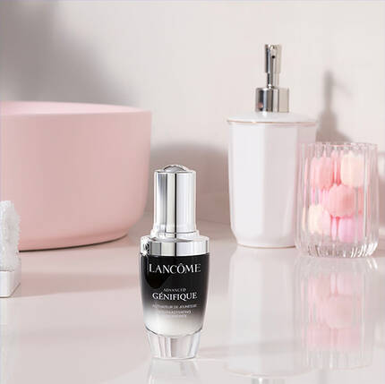 Serum Lancome Genifique na elegantnim stole se skleněnym vazičkou s růži a dalšimi dekorativnimi prvky.