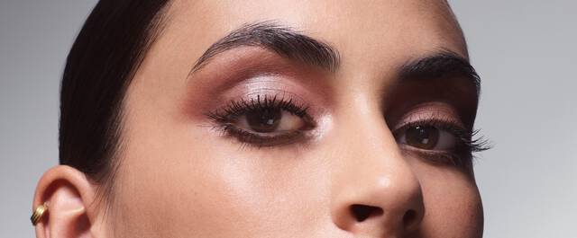 Close-up of a woman's face, focusing on her eyes, which have a soft, smoky eyeshadow and well-defined eyelashes. The background is softly blurred, highlighting her features.