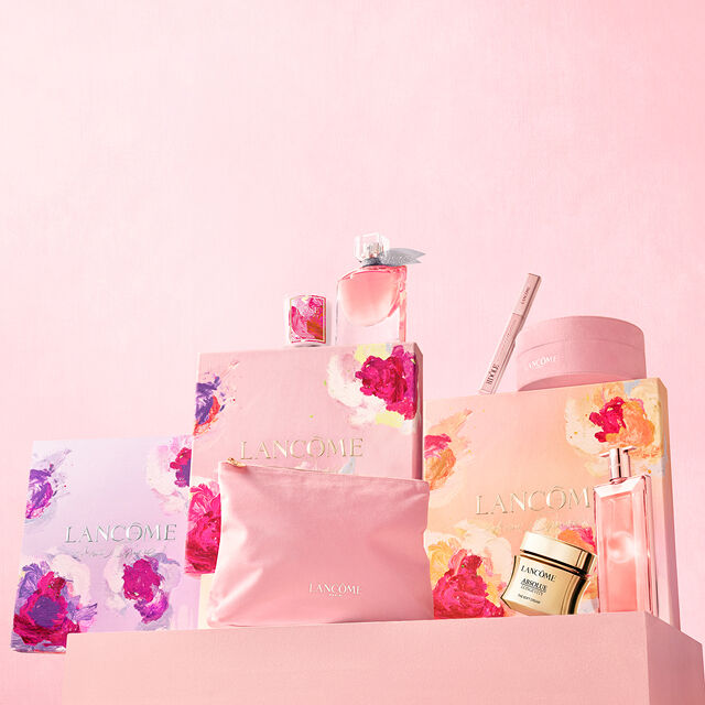 A collection of Lancome beauty products, including perfume and cosmetics, elegantly displayed on a soft pink background with floral patterns on the packaging.