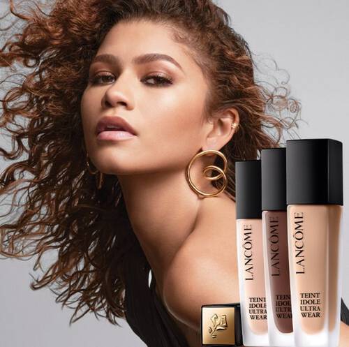 Žena s kudrnatymi vlasy a zlatymi naušnicemi prezentuje produkty značky Lancome.