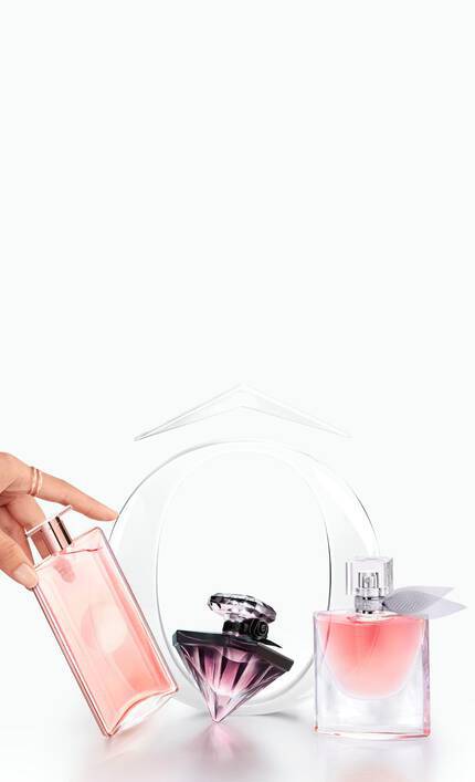 A hand reaching for a pink perfume bottle beside two other elegant perfume bottles against a light pastel background.