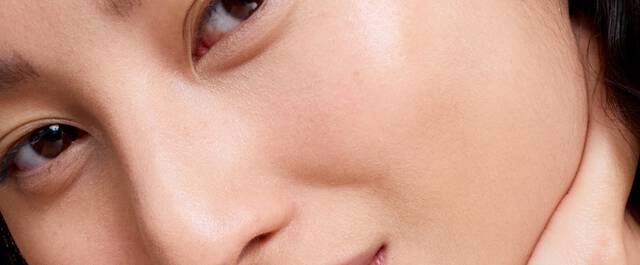 Close-up of a person's face, focusing on their skin and eyes, with a softly lit background.